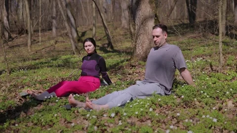 Couple sits on soft green forest clearing carefully performing gentle exercises 库存影片 333267562