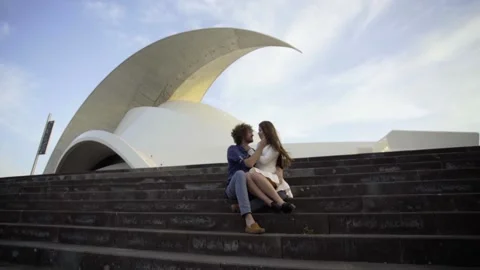 The couple sits on steps in front of the Auditorio de Tenerife amphitheater Stock Footage 219350562