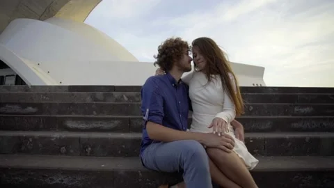 The couple sits on steps in front of the Auditorio de Tenerife amphitheater Stock Footage 229965367