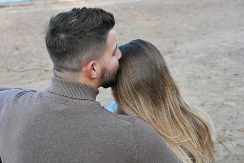 The couple sits with their backs to the camera, the guy kisses the girl's hai Stock Photos