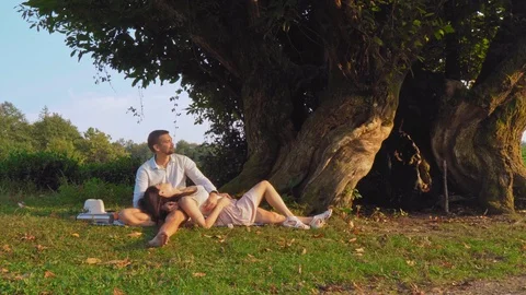 A couple sits under a tree and enjoys nature. A young couple on a picnic on a 스톡 동영상 116326624