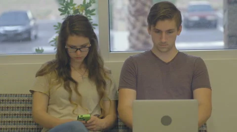 Couple Sits Waiting and Looking at Their Devices Stock Footage 60989315