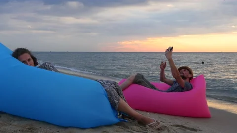 Couple sitting on air bed on beach at sunrise. Man and woman having relaxing Video stock 139980980