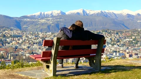 Couple Sitting and Hugging on a Bench and Walking Away with Snowcapped Mountain Stockbeeldmateriaal 194011869