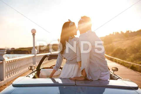 Couple sitting and kissing in cabriolet on sunset Stock Photos