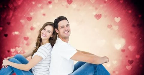 Couple sitting back to back against digitally generated pink background with Stock Photos