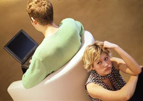 Couple sitting back to back, man on chair using laptop, woman looking up, Stock Photos