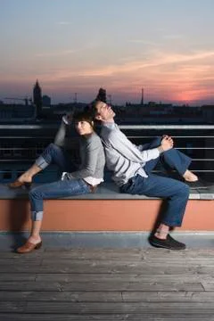 A couple sitting back to back on a rooftop terrace at night 写真素材