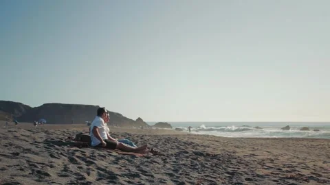 Couple sitting on the beach as the guy points toward the ocean Stock Footage 337465780