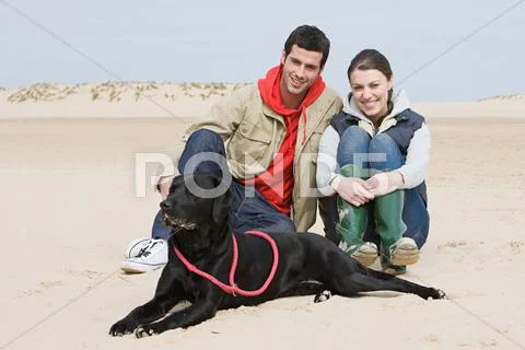 Couple Sitting On Beach With Pet Dog