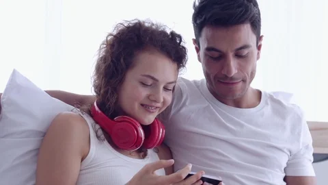 Couple sitting on the bed. A man eating the sandwich at breakfast. A woman liste Видео 107735862