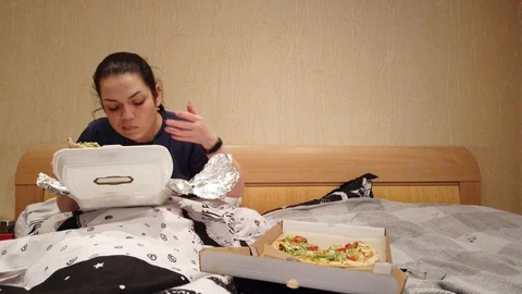 Couple sitting in bed selecting TV show to watch, eating snacks, pizza and havin Stock Footage 105377163