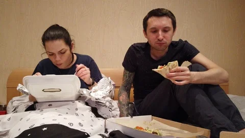 Couple sitting in bed selecting TV show to watch, eating snacks, pizza and havin Stock Footage 105380288