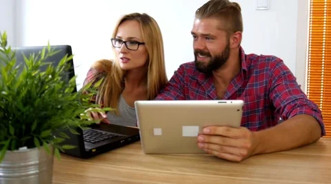 Couple sitting behind the table with tablet pc and laptop. Video stock 54931390