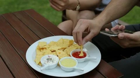 Couple sitting behind table. They are using their smartphones and eating chips Video stock 51440994