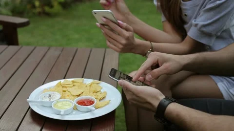Couple sitting behind the table. They are using smartphones and eating chips Stock Footage 51441189