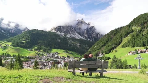 Couple sitting on a bench admiring alpine view of the Dolomites and traditional Vídeo Stock 319920852