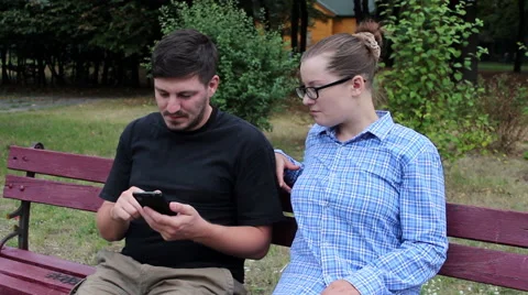 Couple sitting on a bench and uses smartphone Stock Footage 52851399