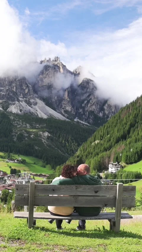 Couple sitting on bench facing mountain range in Dolomites, Italy Stockbeeldmateriaal 319063443