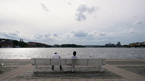 Couple sitting on a bench in front of water body 스톡 동영상 131940052