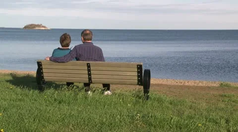 A couple sitting on a bench looking out to a large rock in the ocean (2 of 2 Stock Footage 10775148