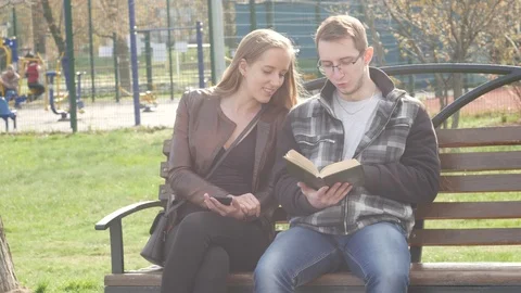Couple is sitting on a bench in the park in the spring and reading an interes Stock Footage 88863054
