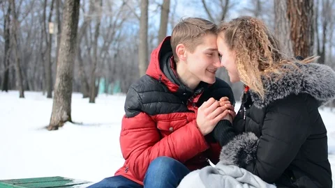 The couple is sitting on a bench in the winter. the guy is heating the girl Stock Footage 88374696