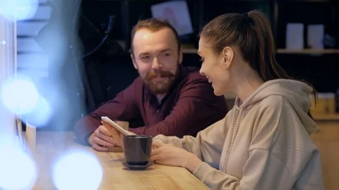 A couple sitting in a cafe, talking, drinks coffee and watching in smartphone. Stock Footage 121835414