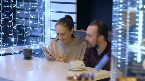 A couple sitting in a cafe, talking, drinks coffee and watching in smartphone. Stock Footage 121835439