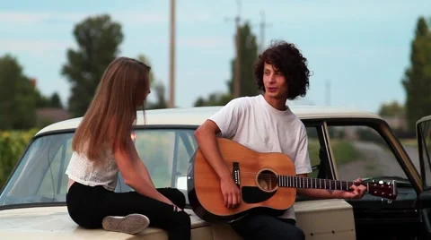Couple Sitting on the Car. the Guy Playing the Guitar For a Girl. Very Stock Footage 67046512