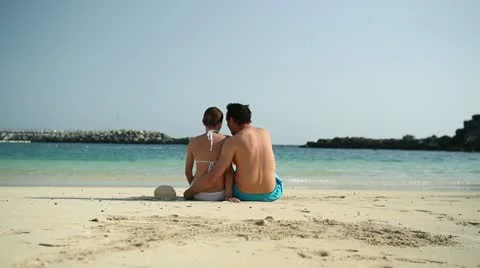 Couple sitting close together on the beach, rear view HD Stock Footage 10901740
