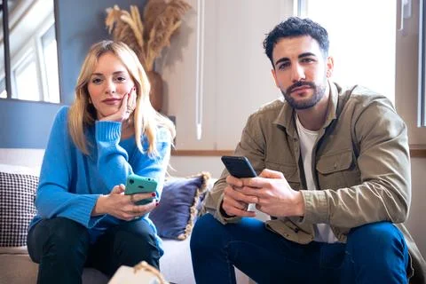 Couple sitting on a comfortable sofa, each with their smartphone in their hand Stock-Fotos