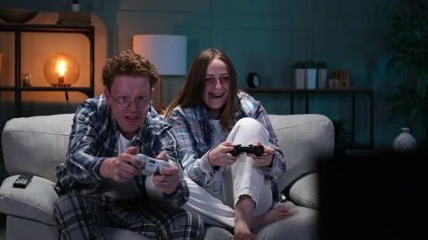Couple sitting on couch playing video games and laughing Stock Footage 166099709