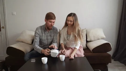 Couple is sitting on the couch sofa at home, Drink tea from a white tea set and Stock Footage 74426986