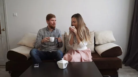 Couple is sitting on the couch sofa at home, Drink tea from a white tea set and Stock Footage 74427569