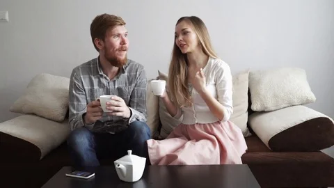 Couple is sitting on the couch sofa at home, Drink tea from a white tea set and Stock Footage 74428429