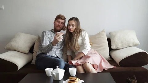 Couple is sitting on the couch sofa at home stroking a cat, Drink tea from a Stock Footage