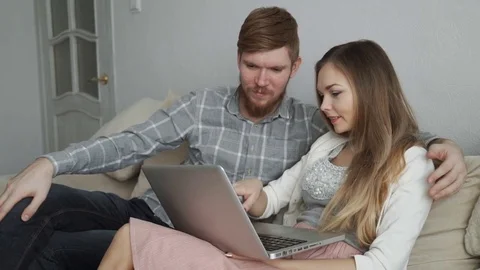 Couple is sitting on the couch sofa at home Look at the laptop screen and smile Stock Footage 74436529