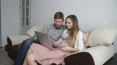 Couple is sitting on the couch sofa at home Look at the laptop screen and smile Stock Footage 74437795