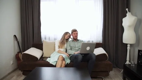 Couple is sitting on the couch sofa at home Look at the laptop screen and smile Stock Footage 74595743