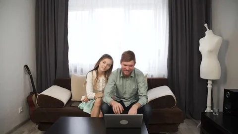 Couple is sitting on the couch sofa at home Look at the laptop screen and smile Stock Footage 74597339