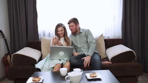 Couple is sitting on the couch sofa at home Look at the laptop screen and smile Stock Footage 74605311