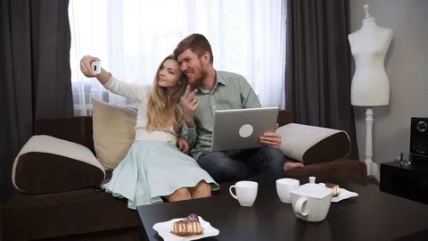 Couple is sitting on the couch sofa at home Do selfie photo on smartphone Look Stock Footage 74606460