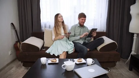 Couple is sitting on the couch sofa at home Look into the tablet and smile Stock Footage 74608656