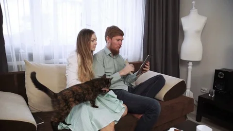 Couple is sitting on the couch sofa at home Look into the tablet and smile Stock Footage 74608797