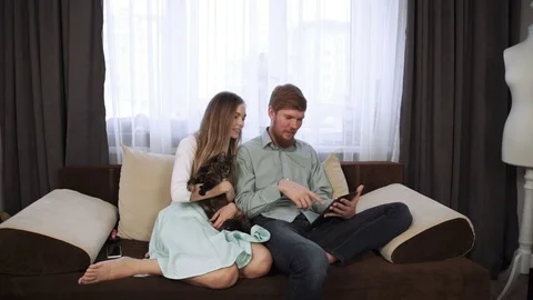Couple is sitting on the couch sofa at home Look into the tablet and smile Stock Footage 74609758