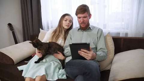 Couple is sitting on the couch sofa at home Look into the tablet and smile Stock Footage 74610666