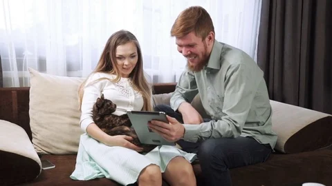 Couple is sitting on the couch sofa at home Look into the tablet and smile Stock Footage 74617260
