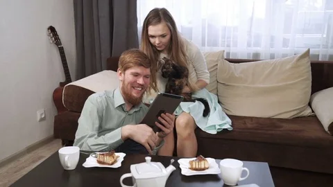 Couple is sitting on the couch sofa at home Look into the tablet and smile Stock Footage 74618806