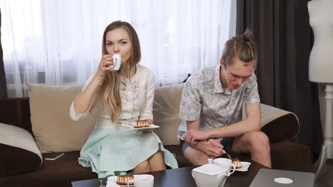 Couple is sitting on the couch sofa at home, Drink tea from a white tea set Stock Footage 74623254